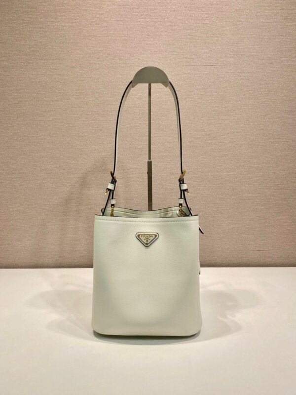 P Home New Bucket Bag 1BE080✨✨ This leather handbag has soft lines and exquisite design, highlighting classic style and handmade details. Practical and versatile, decorated with a triangular metal logo with enamel for added recognition. Leather handle, 28 cm long, removable keychain, metal hardware accessories, enamel triangle metal logo on the front, magnetic buckle closure. Size: 22.5 x 21.5 x 13
