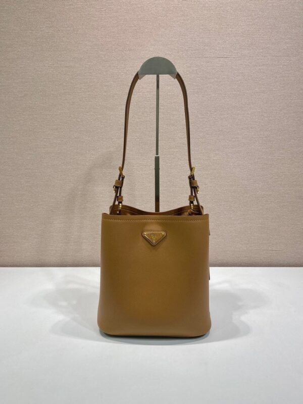 P Home New Bucket Bag 1BE080✨✨ This leather handbag has soft lines and exquisite design, highlighting classic style and handmade details. Practical and versatile, decorated with a triangular metal logo with enamel for added recognition. Leather handle, 28 cm long, removable keychain, metal hardware accessories, enamel triangle metal logo on the front, magnetic buckle closure. Size: 22.5 x 21.5 x 13